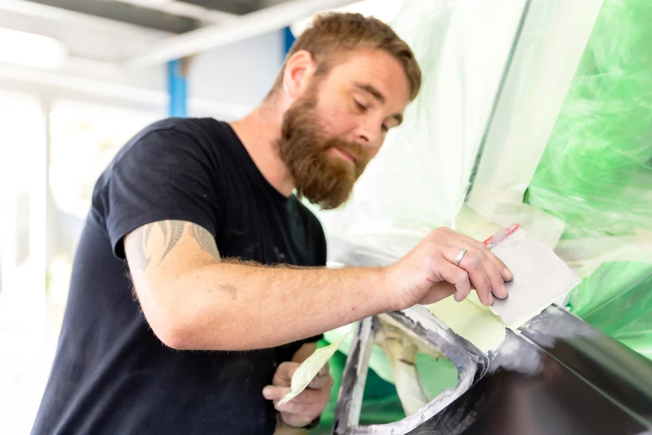 Ein Facharbeiter bereitet eine beschÃ¤digte Stelle an einem Fahrzeug fÃ¼r die Nachlackierung im Rahmen der Unfallinstandsetzung vor.