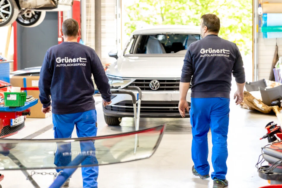 Zwei Werkstattmitarbeiter tragen eine neue Frontscheibe zu einem beschädigten Fahrzeug für den Austausch nach einem Steinschlag oder Unfallschaden.